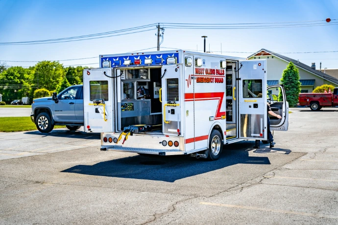 White emergency ambulance with open doors parked on asphalt.